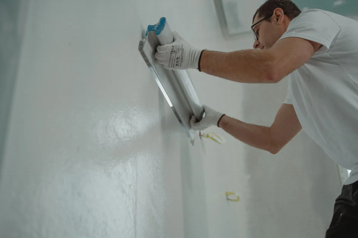 Wide finishing blade drawing a skim coat of joint compound flat across a wall