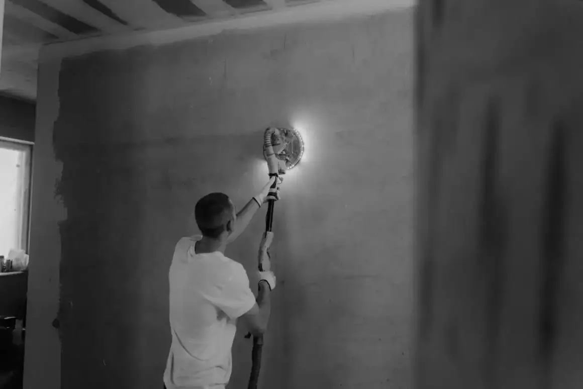 Power sander bringing a coated drywall surface flush during finishing work in Madison