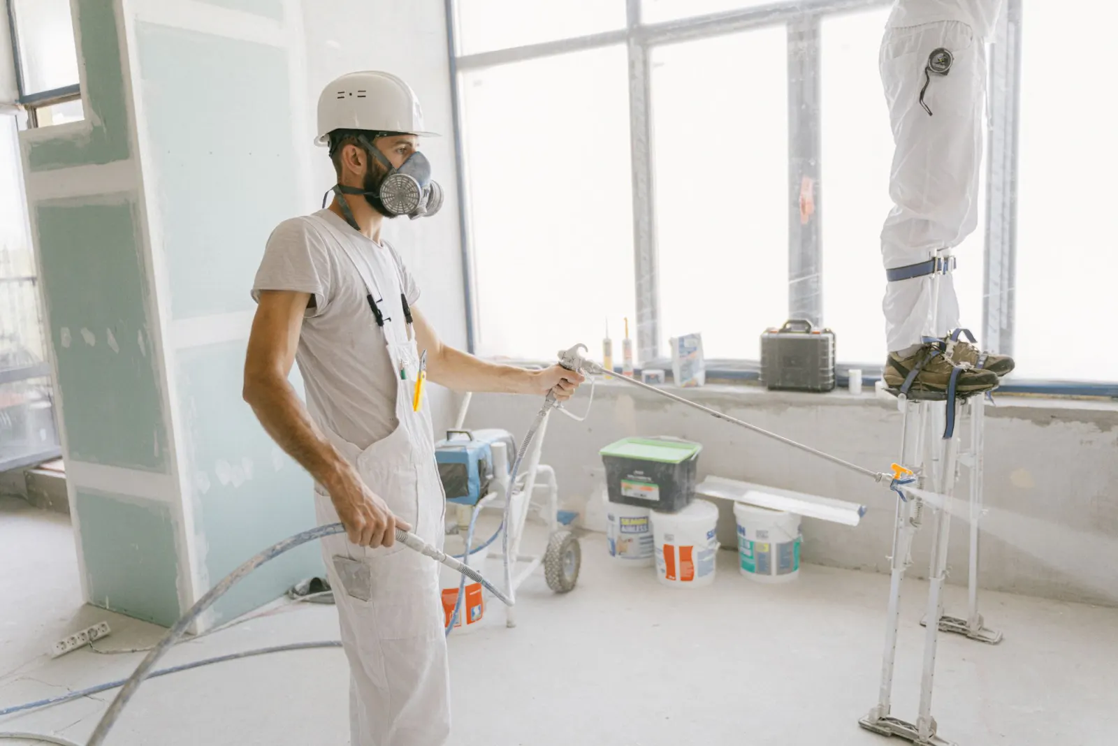 Finish sprayed across a commercial interior while a second worker moves along the ceiling line on stilts